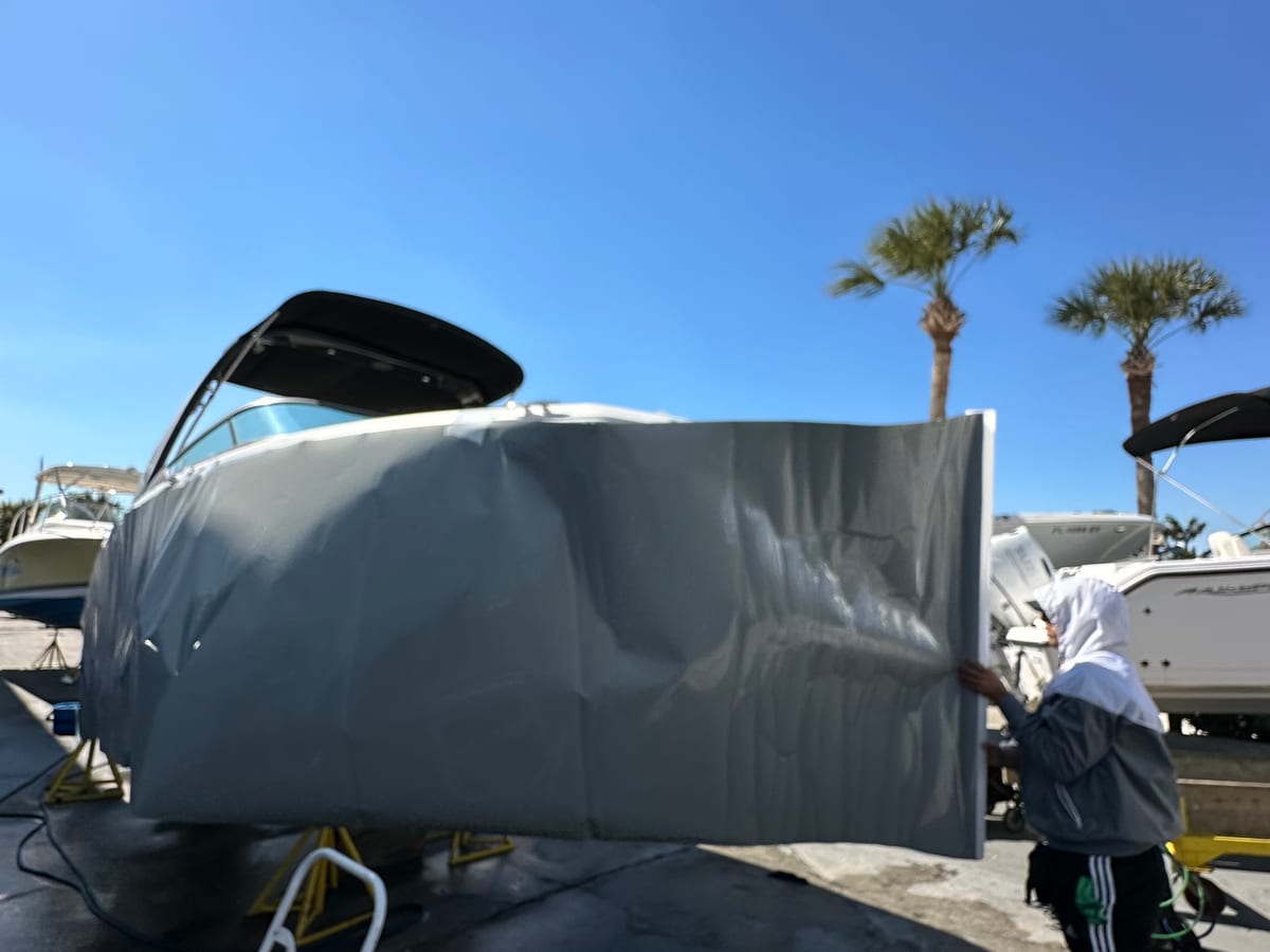 Installer holding a large sheet of gray vinyl against a hull